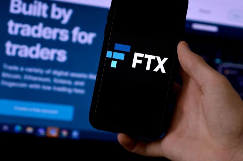 This illustration photo shows a smart phone screen displaying the logo of FTX, the crypto exchange platform, with a screen showing the FTX website in the background in Arlington, Virginia on February 10, 2022. - Sam Bankman-Fried donned a suit and tie this week, abandoning his preferred hoodie and dark T-shirt for a hearing before US Senators. The lawmakers had summoned the 29-year-old multi-billionaire on Wednesday to discuss the regulation of digital assets in his capacity as co-founder and CEO of the cryptocurrency exchange platform FTX (Photo by OLIVIER DOULIERY / AFP) (Photo by OLIVIER DOULIERY/AFP via Getty Images)