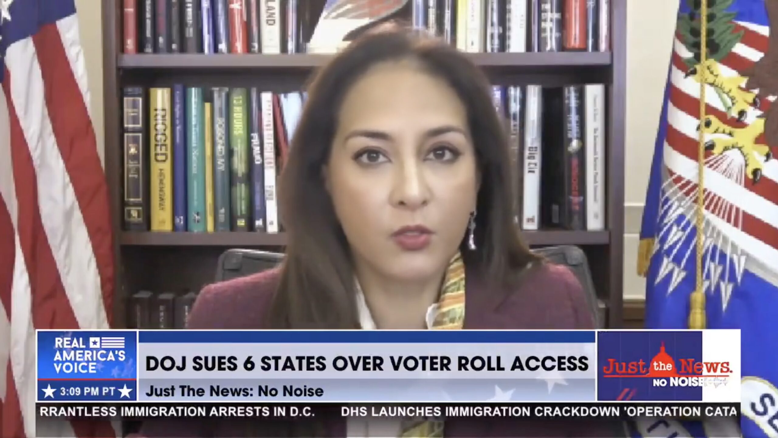 DOJ official discusses the lawsuit against six states regarding voter roll access, with a U.S. flag and books in the background.