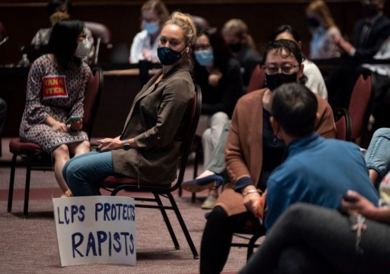 A woman sits with her sign during a Loudoun County Public Schools (LCPS) board meeting in Ashburn, Virginia on October 12, 2021. - Loudoun county school board meetings have become tense recently with parents clashing with board members over transgender issues, the teaching of critical race theory (CRT) and Covid-19 mandates. Recently tensions between groups of parents and the school board increased after parents say an allegedly transgender individual assaulted a girl at one of the schools. Earlier this month US Attorney General Merrick Garland directed federal authorities to hold strategy sessions in the next month with law enforcement to address the increasing threats targeting school board members, teachers and other employees in the nation's public schools. This in response to a request from the National School Boards Association asking US President Joe Biden for federal assistance to investigate and stop threats made over policies including mask mandates, likening the vitriol to a form of domestic terrorism. (Photo by Andrew CABALLERO-REYNOLDS / AFP) (Photo by ANDREW CABALLERO-REYNOLDS/AFP via Getty Images)