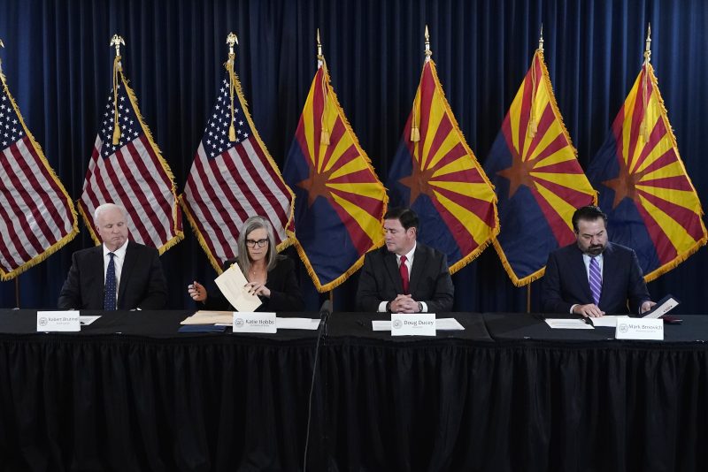 Katie Hobbs, the Democratic governor-elect and current secretary of state, second from left, signs the official certification for the Arizona general election canvass in a ceremony as Arizona Republican Gov. Doug Ducey, second from right, Arizona Supreme Court Chief Justice Robert Brutinel, left, and Arizona Attorney General Mark Brnovich flank Hobbs at the Arizona Capitol in Phoenix, Monday, Dec. 5, 2022. (AP Photo/Ross D. Franklin, Pool)